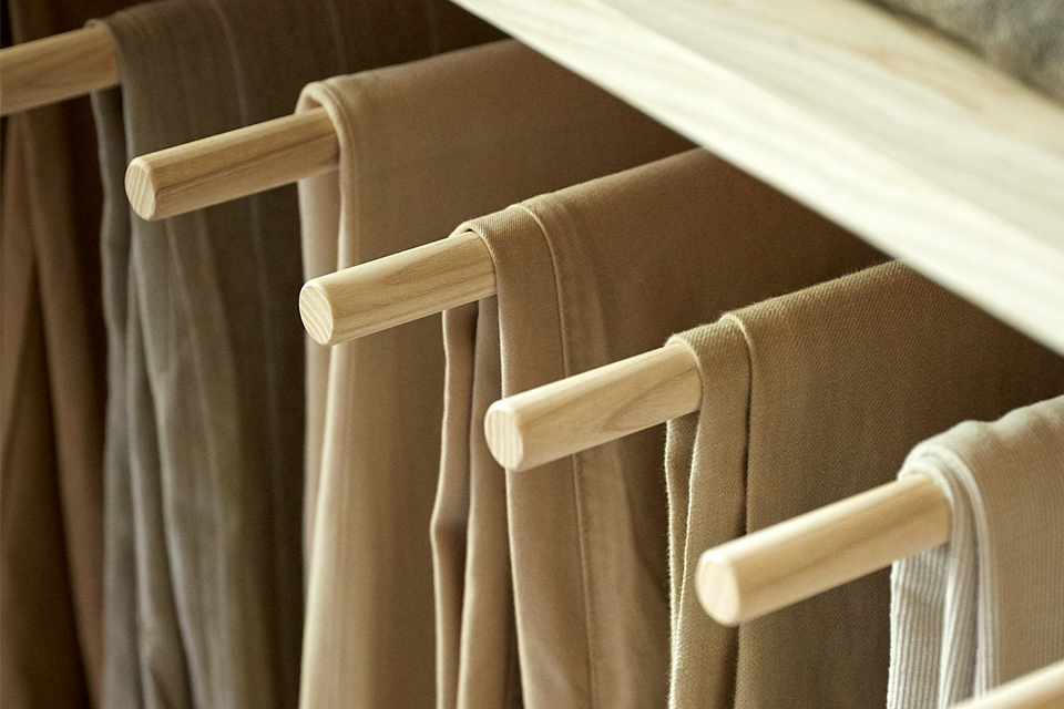 Neutrale Hosen hängen geordnet auf Holzstangen im Schrank