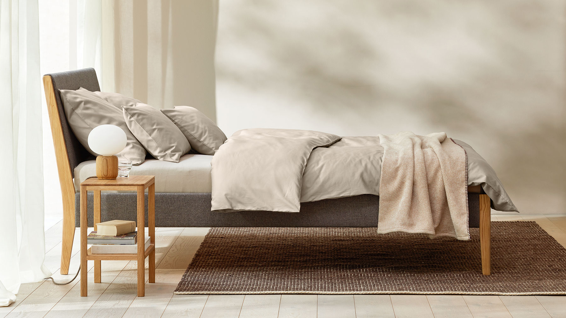 Minimalistisches Bett mit neutralen Textilien in sanfter Beleuchtung