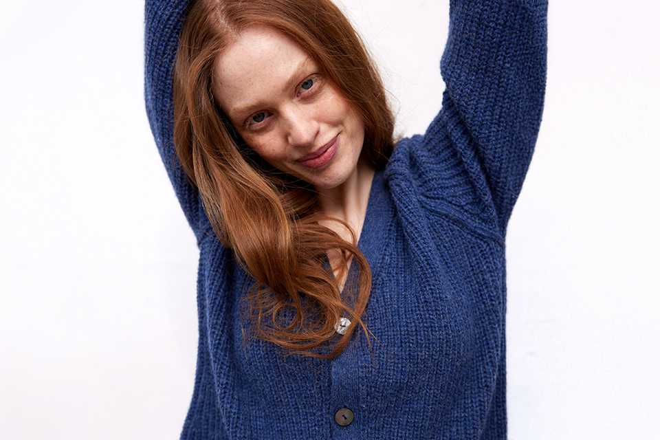 Porträt einer lächelnden Person mit rotem Haar im blauen Pullover