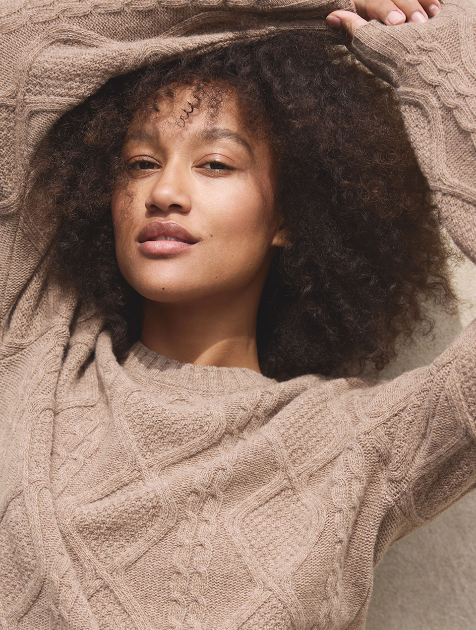Frau mit dunklen Locken trägt braunen Pullover