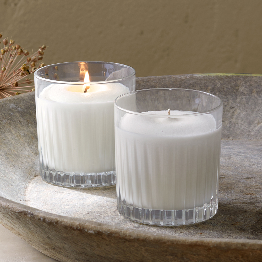 Zwei weiße Kerzen im Glas stehen nebeneinander auf einer Steinschale mit dekorativem Zweig