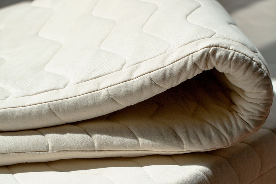 Ein gefalteter Matratzentopper liegt auf einer Naturmatratze