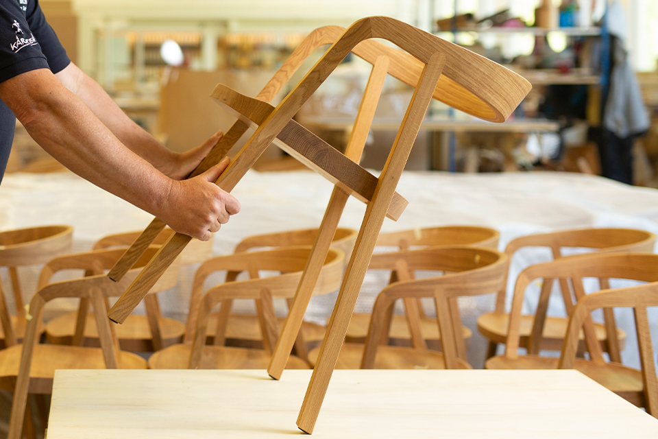 Zwei Hände halten einen Massivholzstuhl in einer Tischlerei