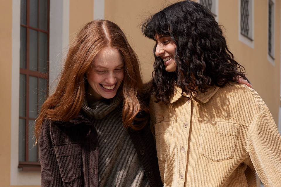 Zwei Frauen gehen Arm in Arm und lachen zusanne,