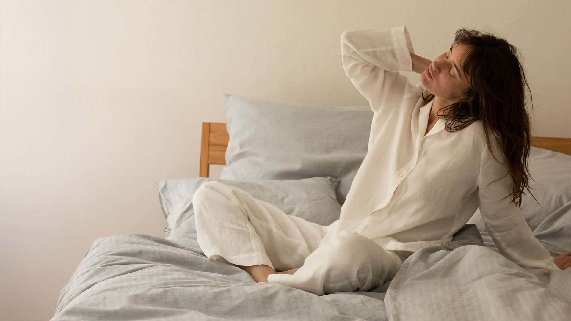 Frau in weißem Pyjama sitzt auf einem Bett