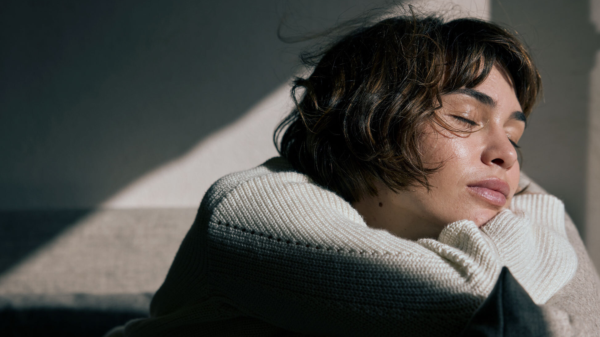 Dunkelhaarige Frau mit geschlossenen Augen und einem hellen Strickpullover