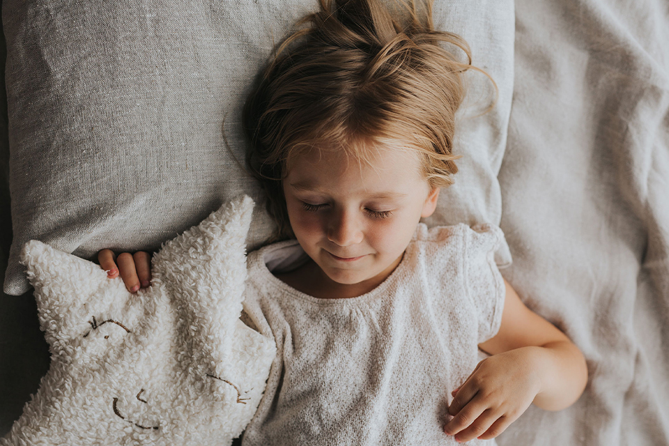 Kind liegt im Bett mit Kuschelkissen