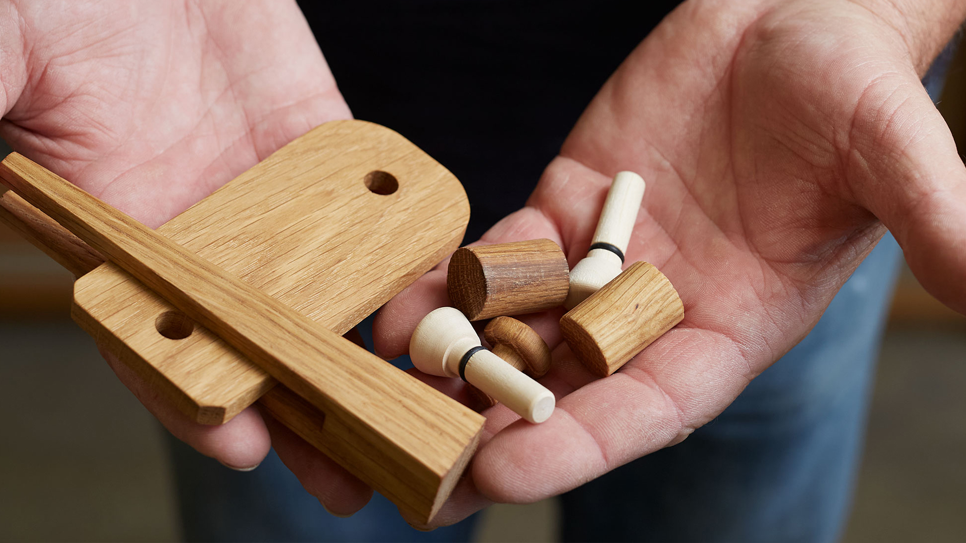 zwei Hände die verschiedene handgefertigte Holzkleinteile präsentieren.