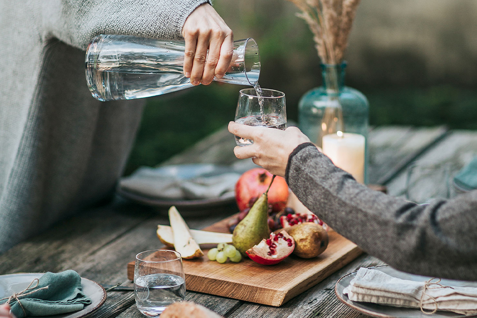 Hände gießen Wasser über frisches Essen auf gedecktem Tisch