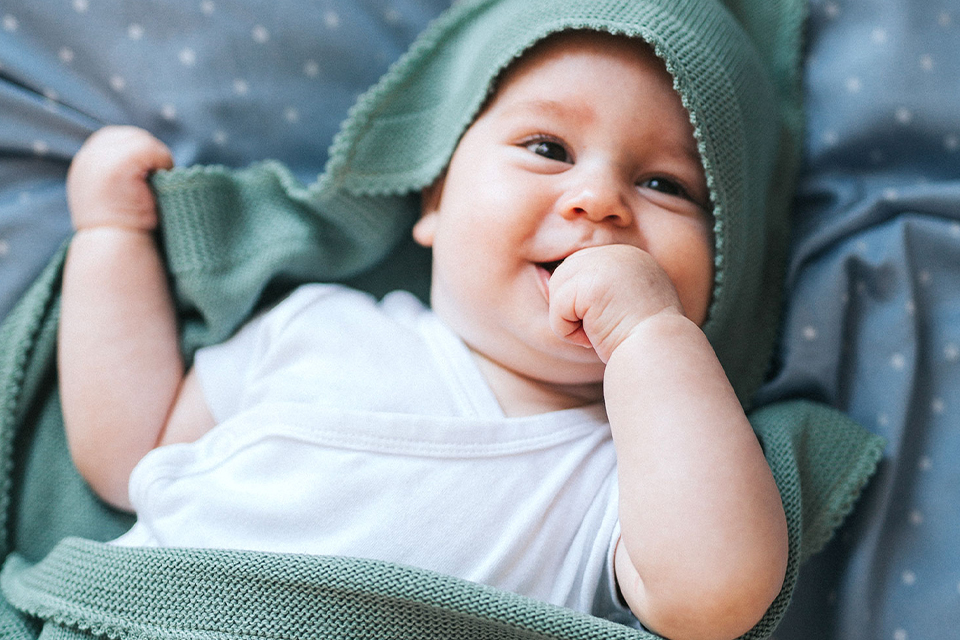 Baby mit grüner Decke lächelt und nuckelt an der Hand