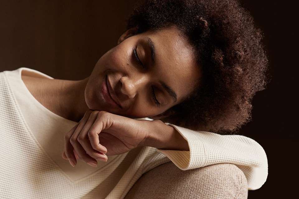 Frau lehnt entspannt auf Sofa und wirkt ruhig und gelöst