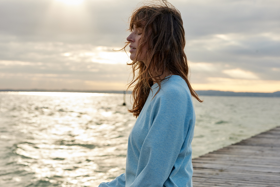 Frau steht am Meer und blickt ruhig in die Ferne