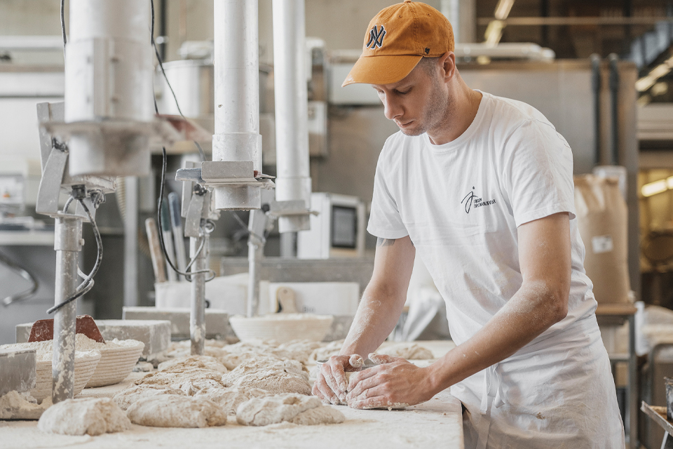 Bäcker knetet Teig in moderner Backstube mit Maschinen