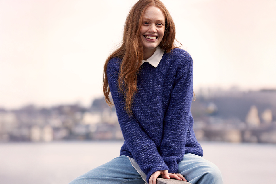 Lächelnde Frau im blauen Pullover mit unscharfem Hintergrund