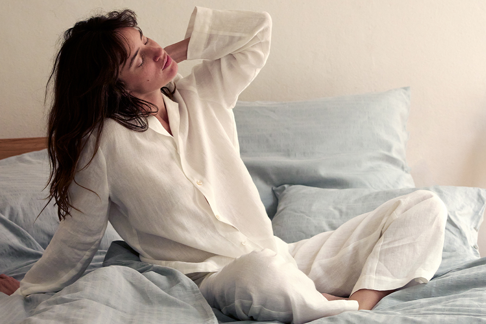 Eine Frau mit weißem Pyjama in einem Bett mit hellblauer Bettwäsche