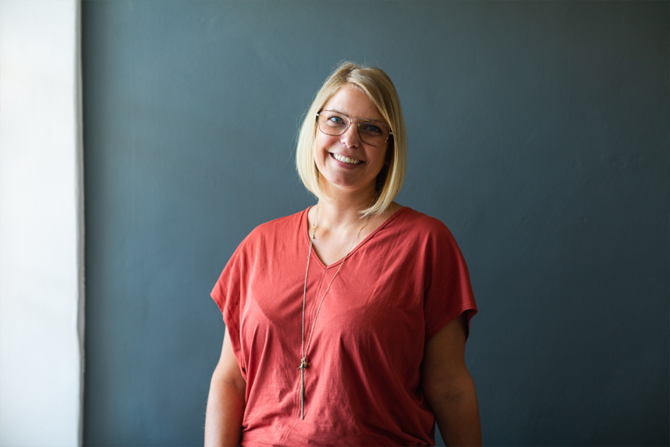 Frau steht lächelnd vor ruhigem Hintergrund und blickt in die Kamera