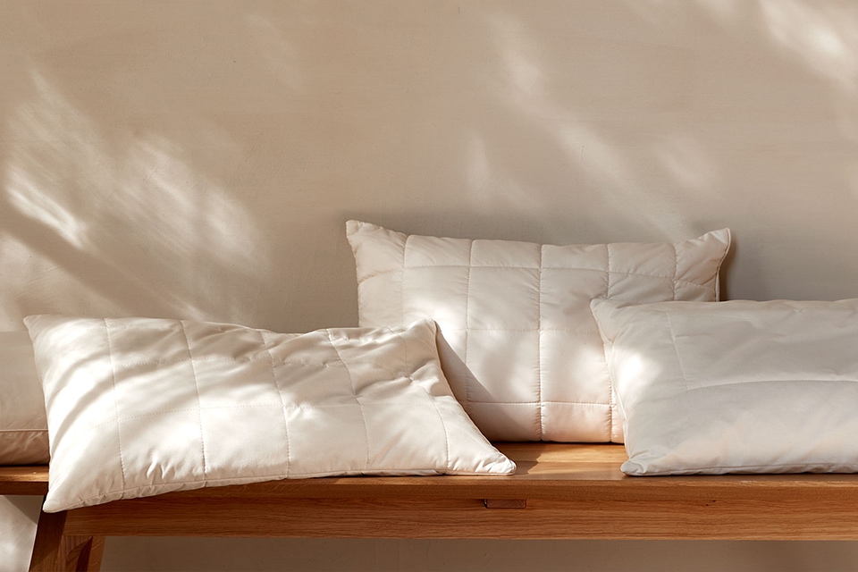 Drei hochwertige Schlafkissen liegen auf einer Holzbank