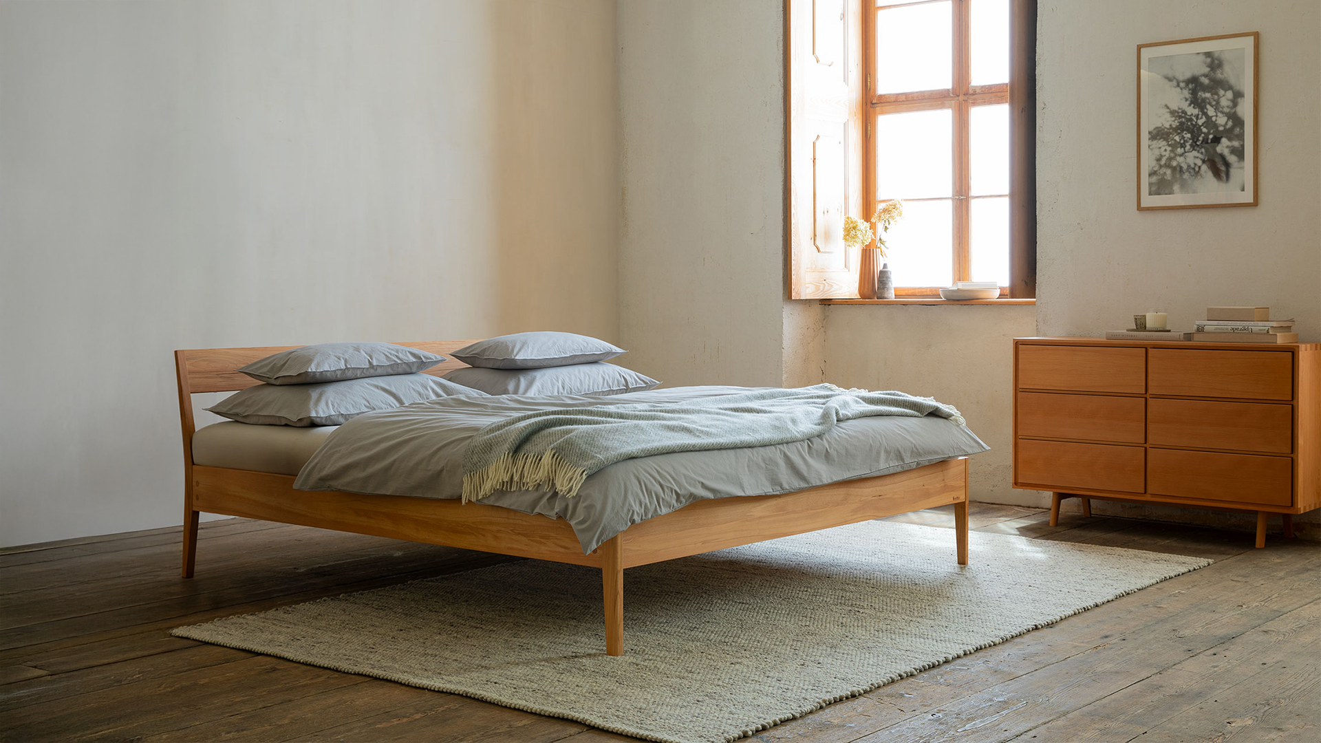 Massivholzbett und Kommode vor einem Fenster